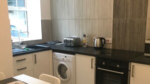 Une cuisine compacte équipée d’un lave-linge, d’un grille-pain et d’une bouilloire posés sur le plan de travail.