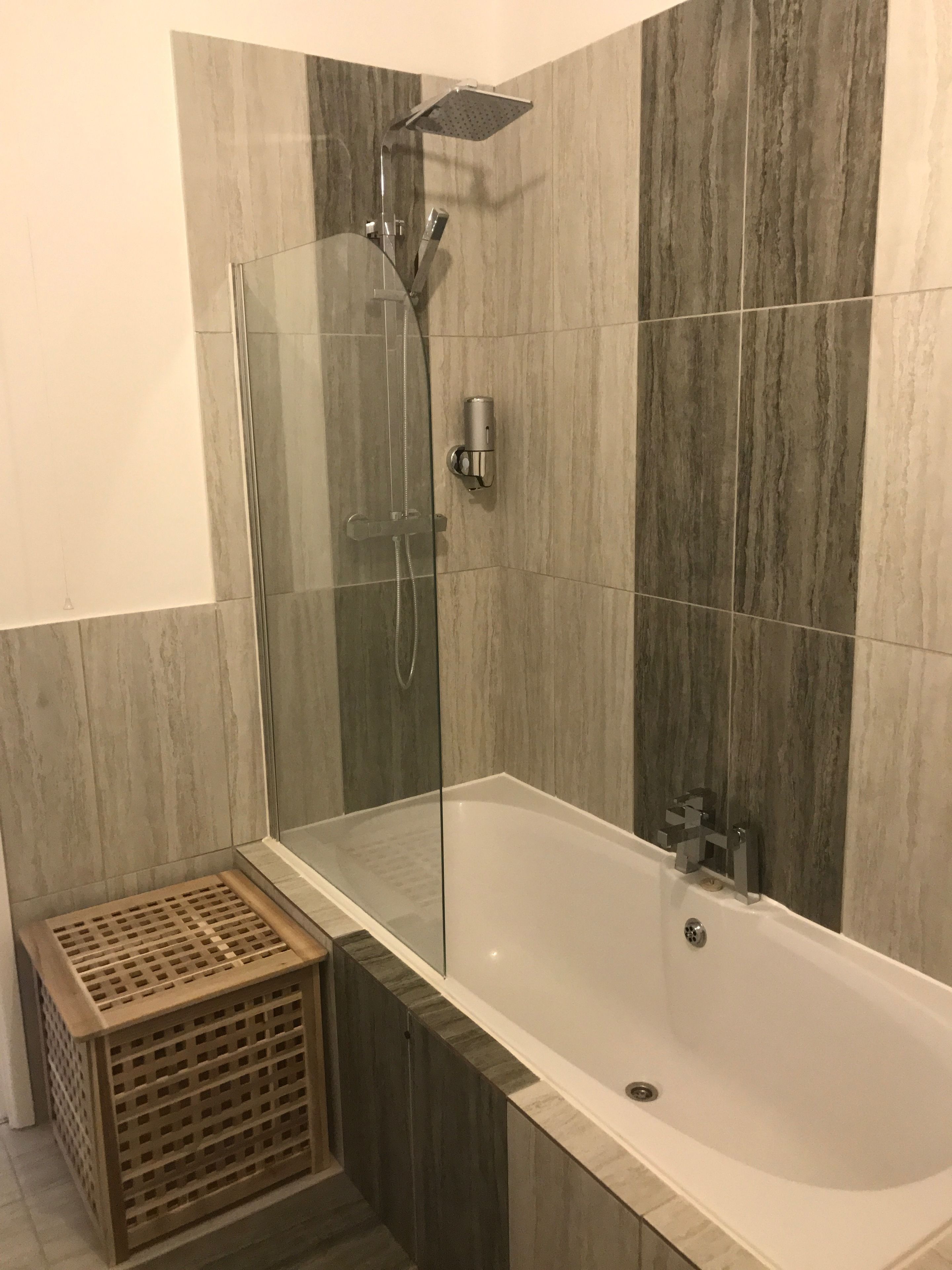 A modern bathroom with a glass-enclosed shower, a freestanding bathtub, and a wooden laundry basket.