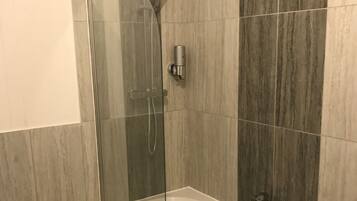 A modern bathroom with a glass-enclosed shower, a freestanding bathtub, and a wooden laundry basket.