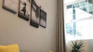 Un canapé gris avec des coussins jaunes, une plante en pot et trois œuvres d’art accrochées au mur.