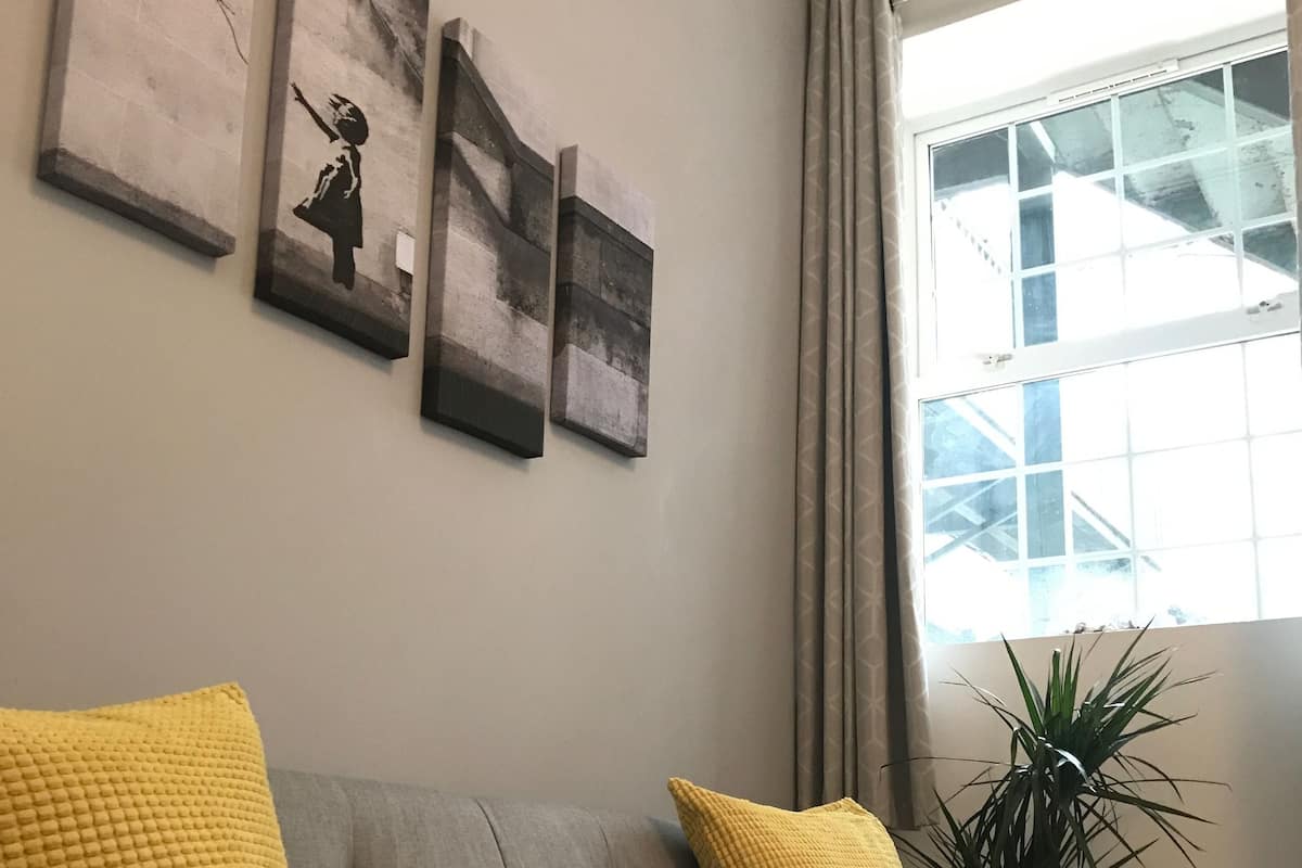 A grey sofa with yellow cushions, a potted plant, and three wall-mounted artworks.
