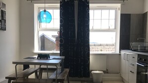 Une cuisine compacte avec un coin repas, une fenêtre avec des rideaux, un radiateur et une suspension bleue.