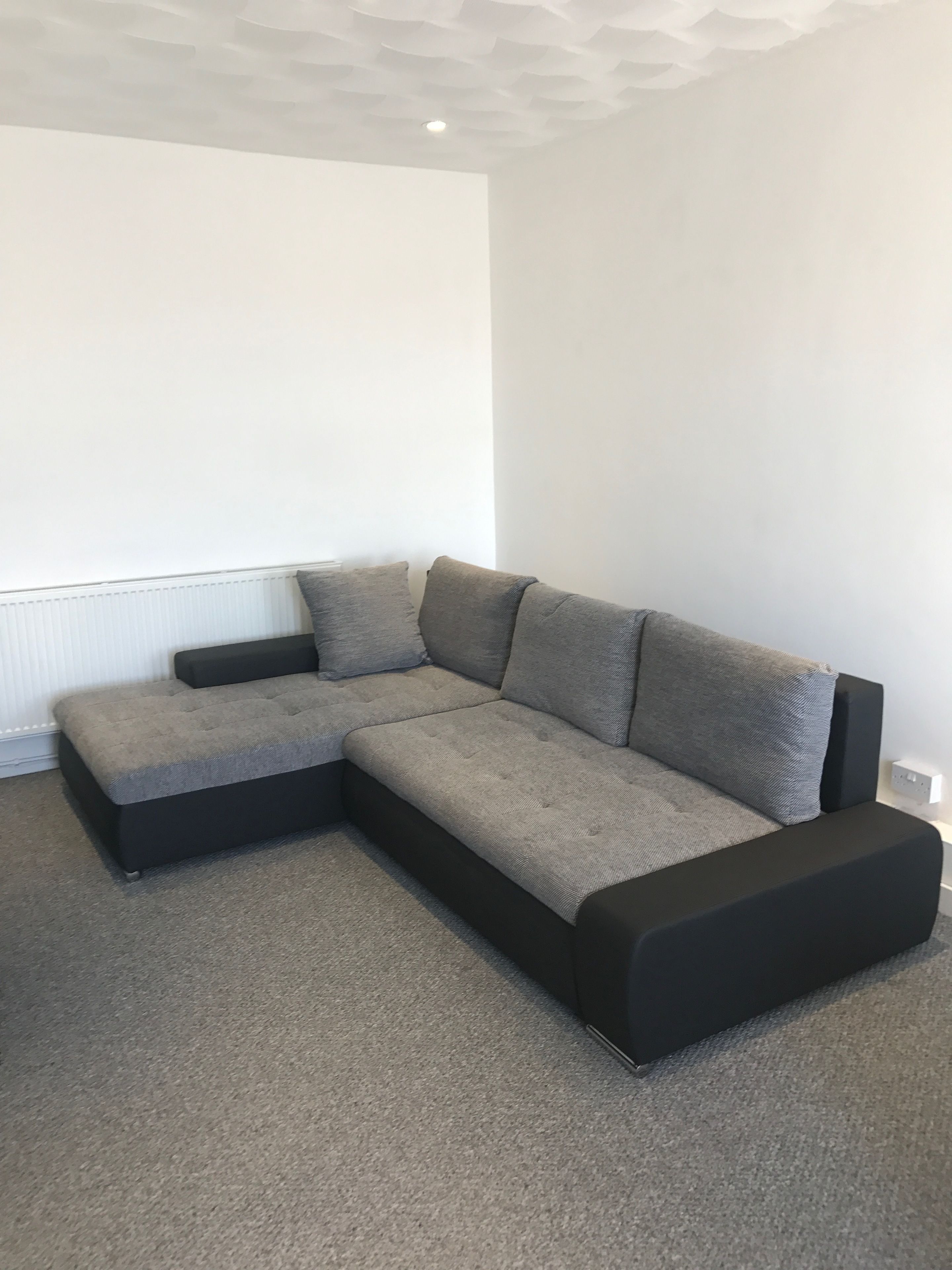 A sectional sofa with a black and grey color scheme, positioned against a white wall with a recessed ceiling.