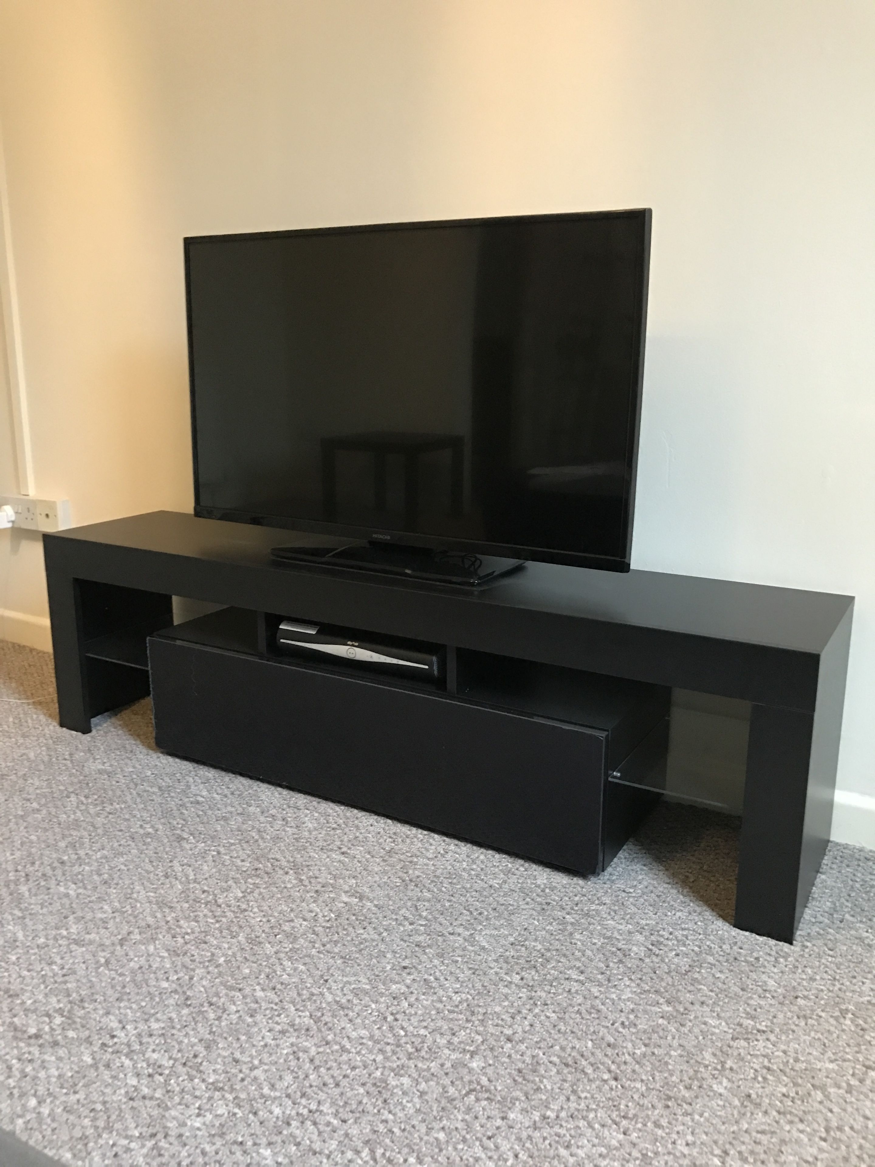 Un mueble multimedia negro con televisor de pantalla plana, una mesita y un cajón.