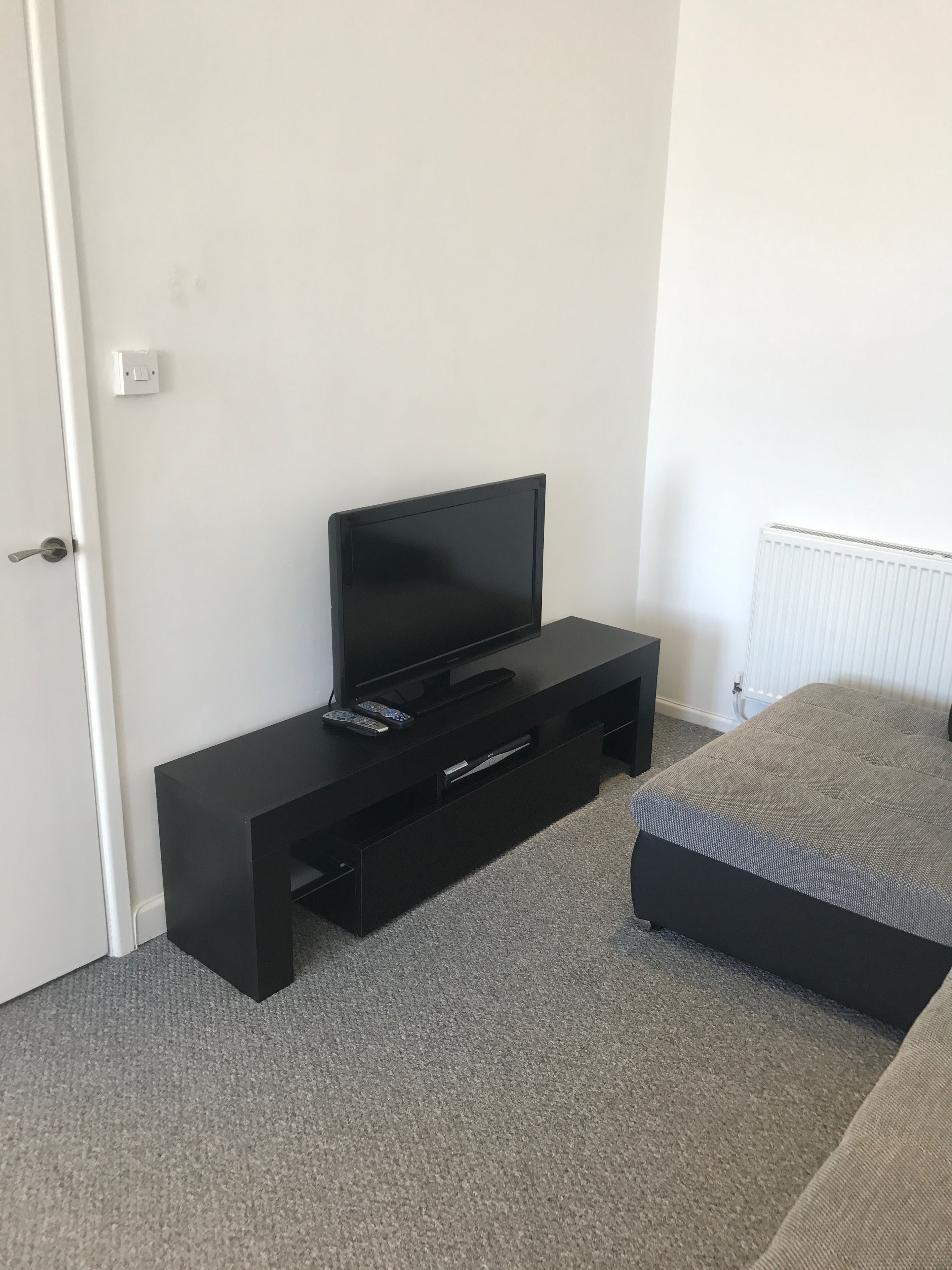 Un dormitorio con un mueble negro para televisor, una cama y una puerta blanca.