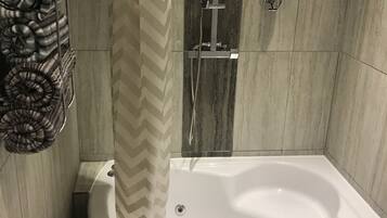 Un baño moderno con una bañera independiente, un cabezal de ducha y un perchero con una toalla estampada.