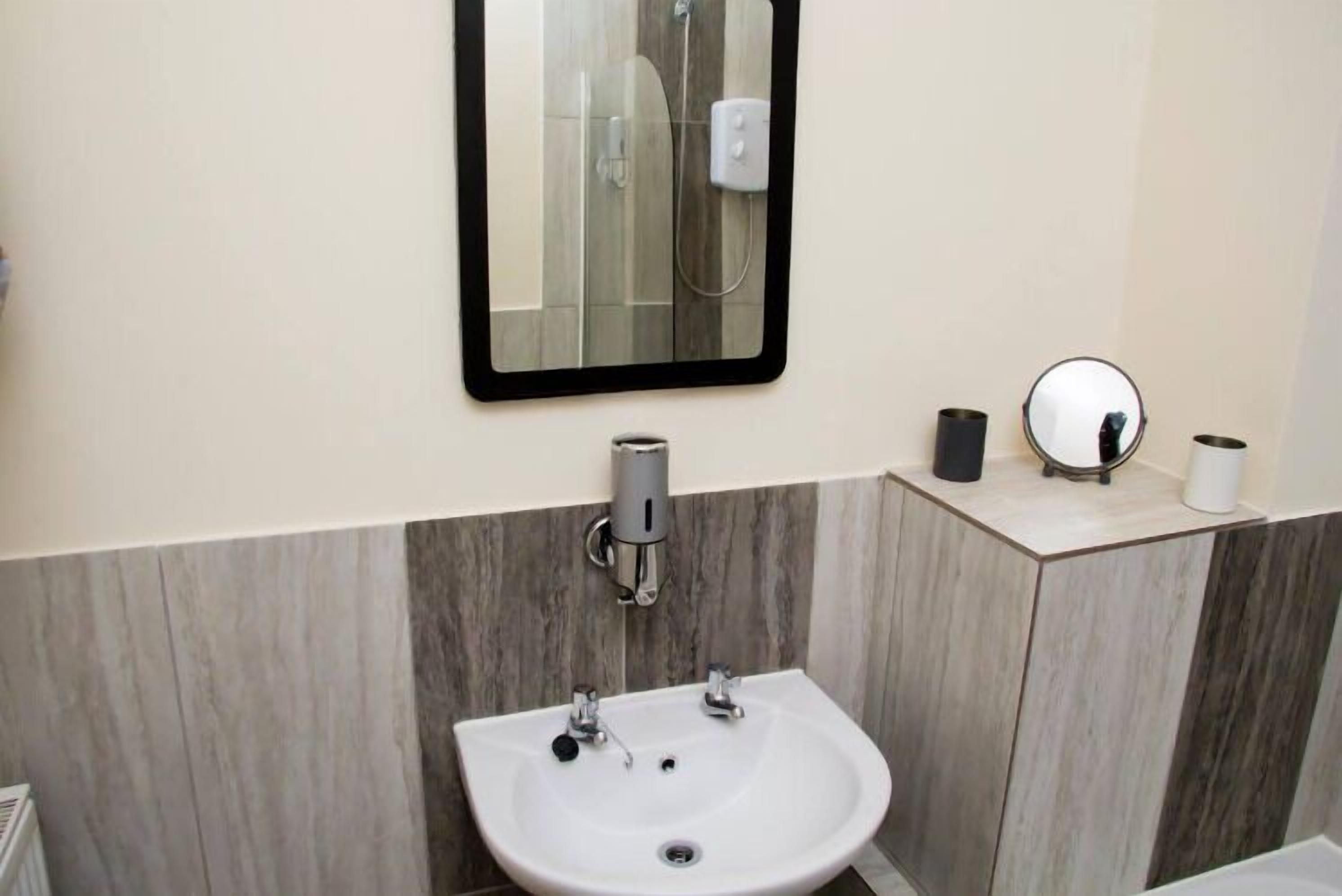 A bathroom with a white sink, two faucets, a mirror, and a towel dispenser.