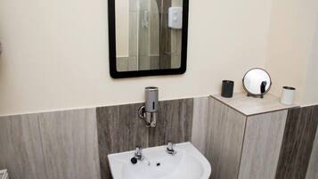 A bathroom with a white sink, two faucets, a mirror, and a towel dispenser.