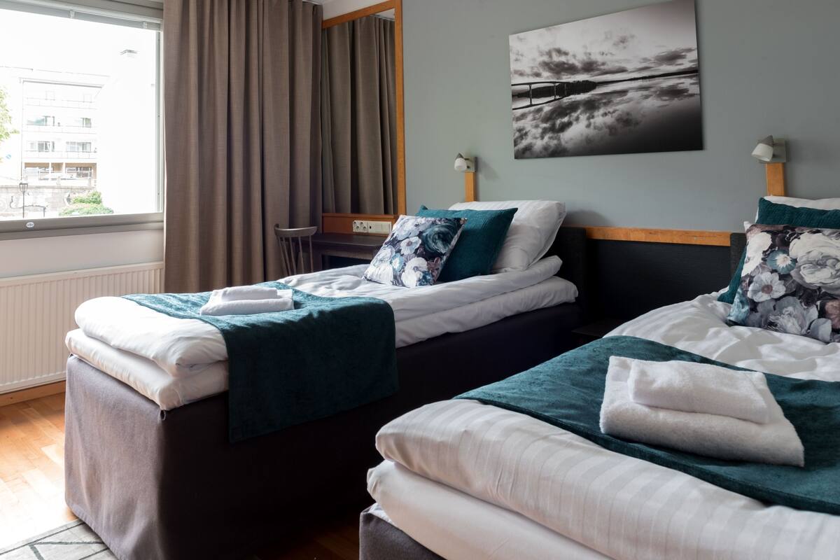 A hotel room with two beds, a desk, and a window with curtains.