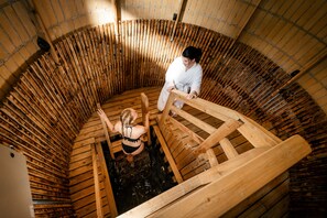 A traditional wooden bathhouse with a circular wooden structure and a person standing inside. - Hotelli Lähde (Lappeenranta)