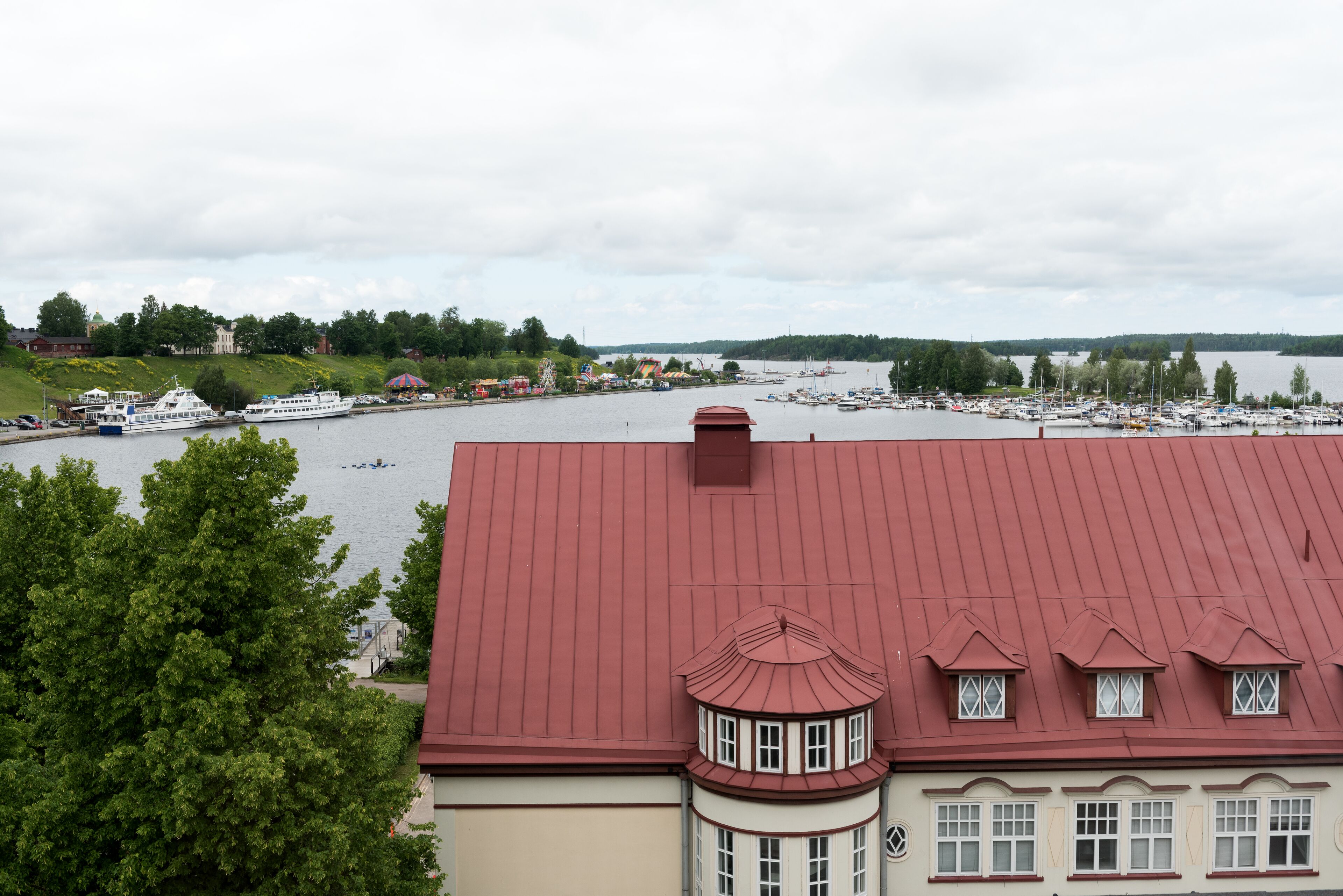Vesirajassa sijaitseva kiinteistö, jossa on punainen katto, lahti täynnä veneitä ja näkymä vesistölle.