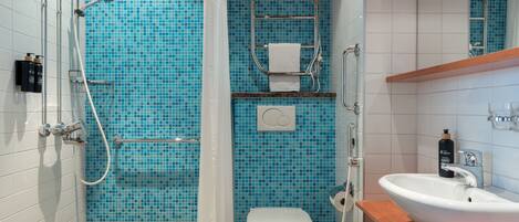 Un baño con pared de mosaicos azules, inodoro blanco, lavamanos con encimera de madera y ducha con puerta de vidrio.