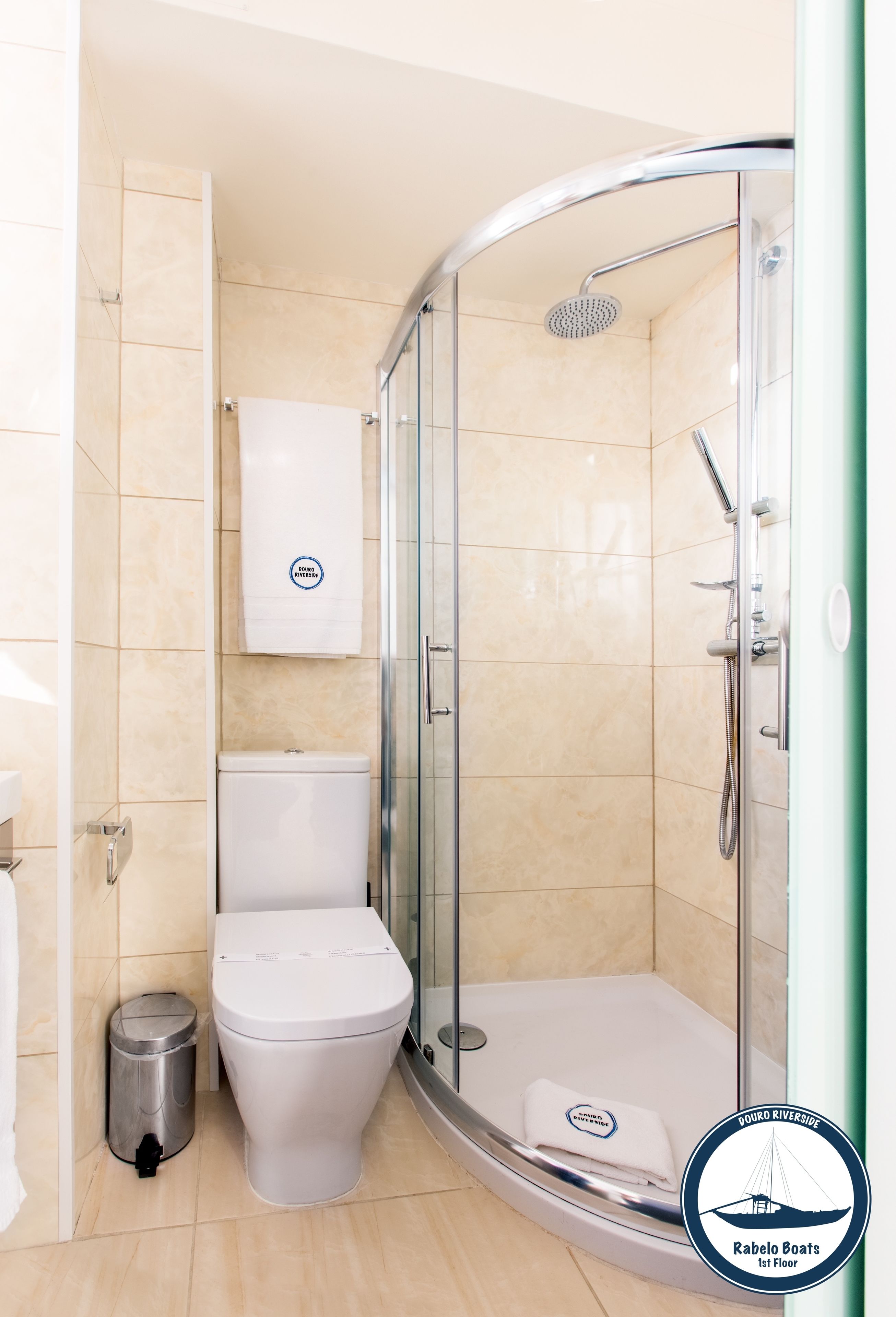 A modern bathroom with a glass-enclosed shower, a white toilet, and a trash bin.