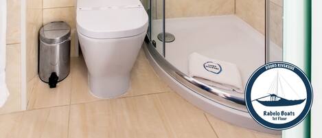 A modern bathroom with a glass-enclosed shower, a white toilet, and a trash bin.