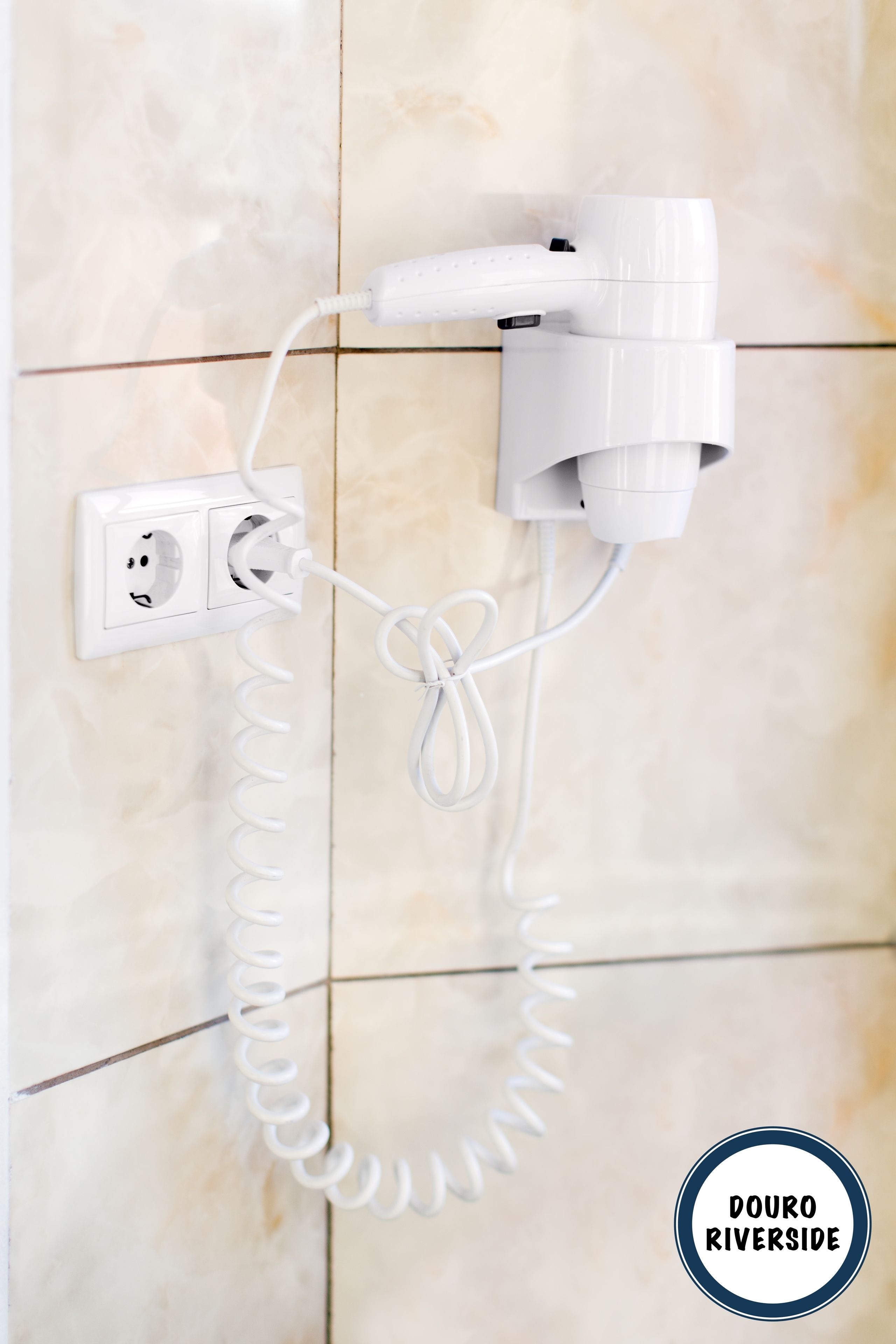 A hairdryer plugged into a wall socket with a coiled cord.