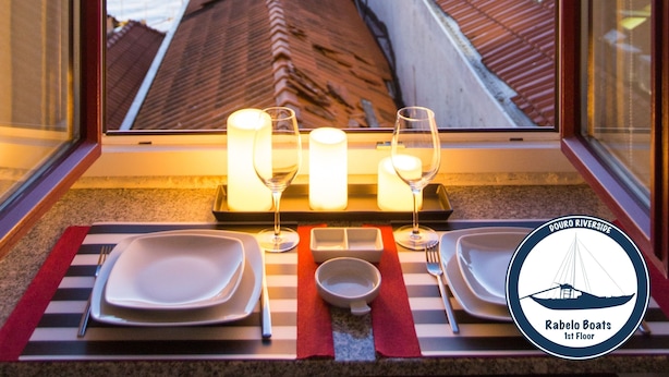 A dining table set with plates, glasses, and candles, overlooking a river with city lights in the background. - Douro Riverside Apartments (Vila Nova de Gaia)