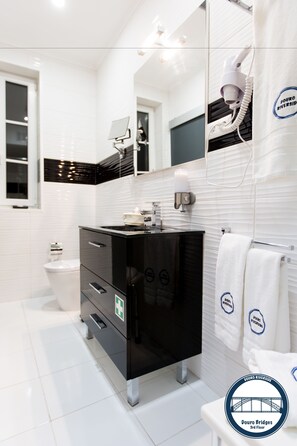 A modern bathroom with a black vanity, white tiles, a mirror, and a towel rack. - Douro Riverside Apartments (Vila Nova de Gaia)