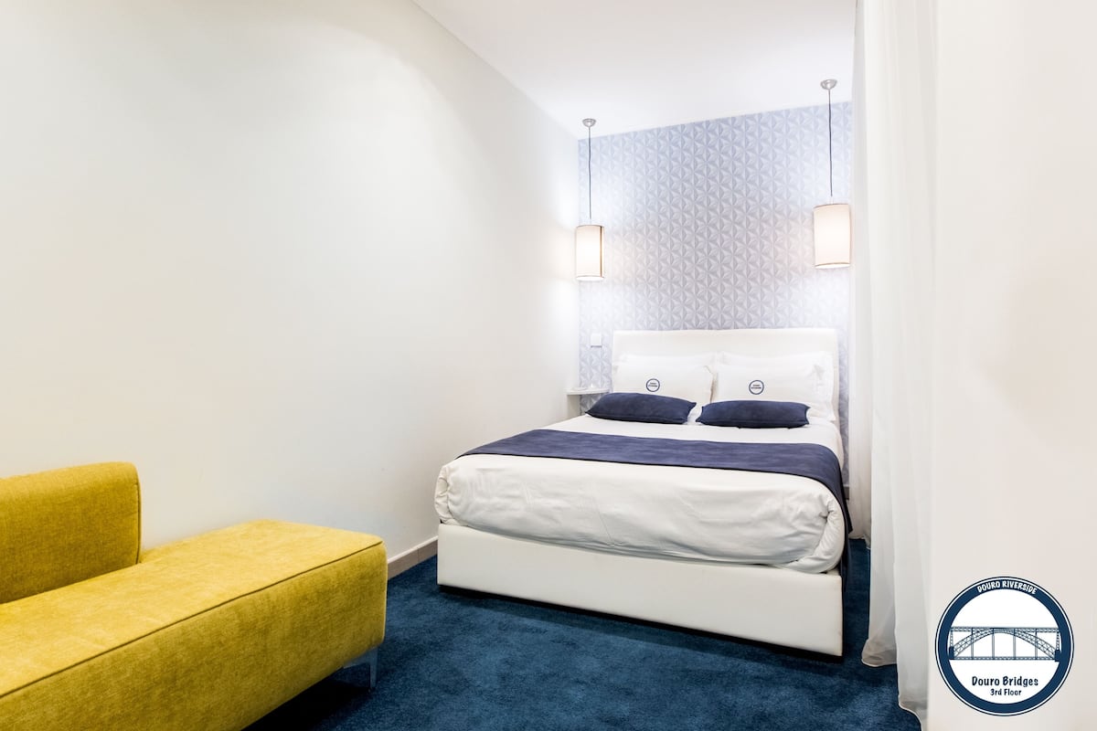 A hotel room with a bed, a yellow sofa, and a patterned wall.