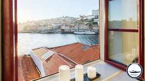 A view from a window overlooking a harbor with boats, a cityscape, and a building with a clock tower. - Douro Riverside Apartments (Vila Nova de Gaia)