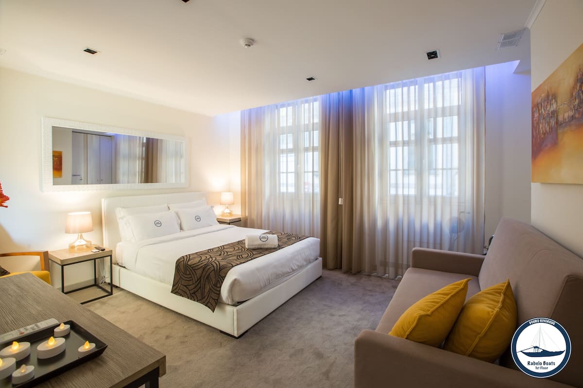A hotel room with a bed, bedside tables, a sofa, and a large window with curtains.