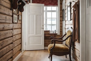 A log cabin interior with a wooden door, a bench, and a window with curtains. - Eggedal Borgerstue (Sigdal)