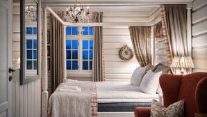 Un dormitorio con una cama con dosel, un candelabro, una ventana con cortinas y un sillón rojo.