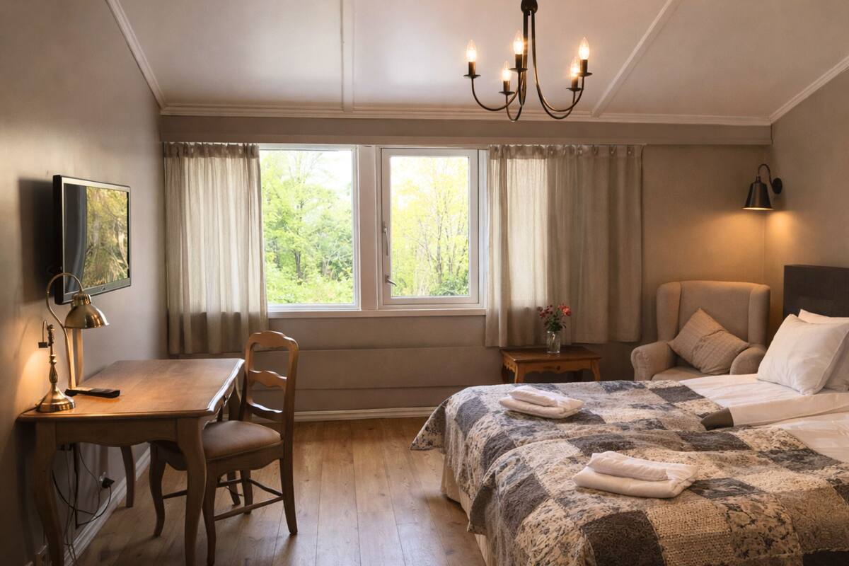 A bedroom with a bed, a desk, a chair, a television, and a window with curtains.