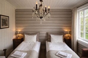 A hotel room with two beds, a chandelier, bedside lamps, a window with a view, and a framed picture on the wall. - Eggedal Borgerstue (Sigdal)