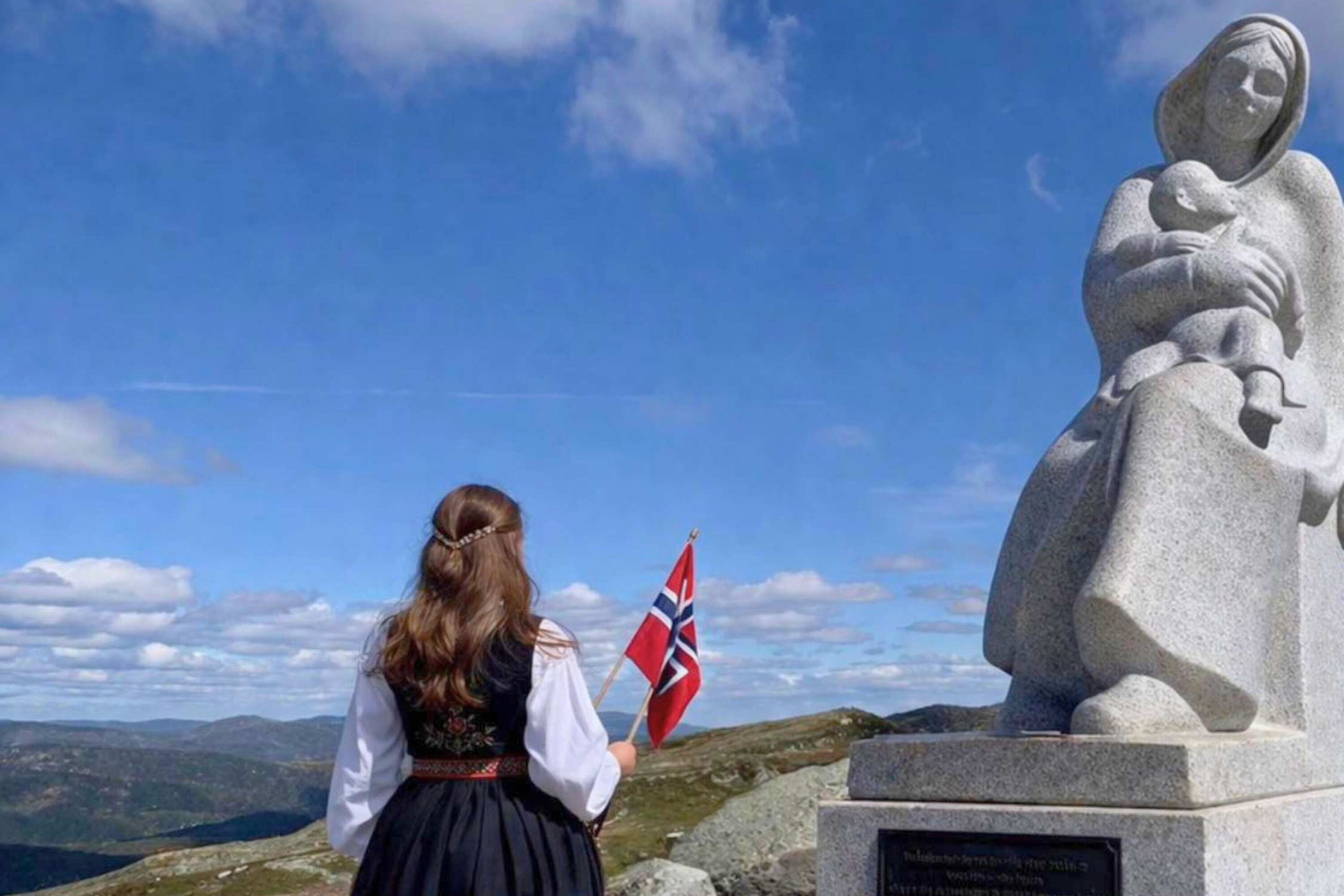 Una estatua de una mujer sosteniendo a un niño, con un cielo despejado y un paisaje montañoso al fondo.