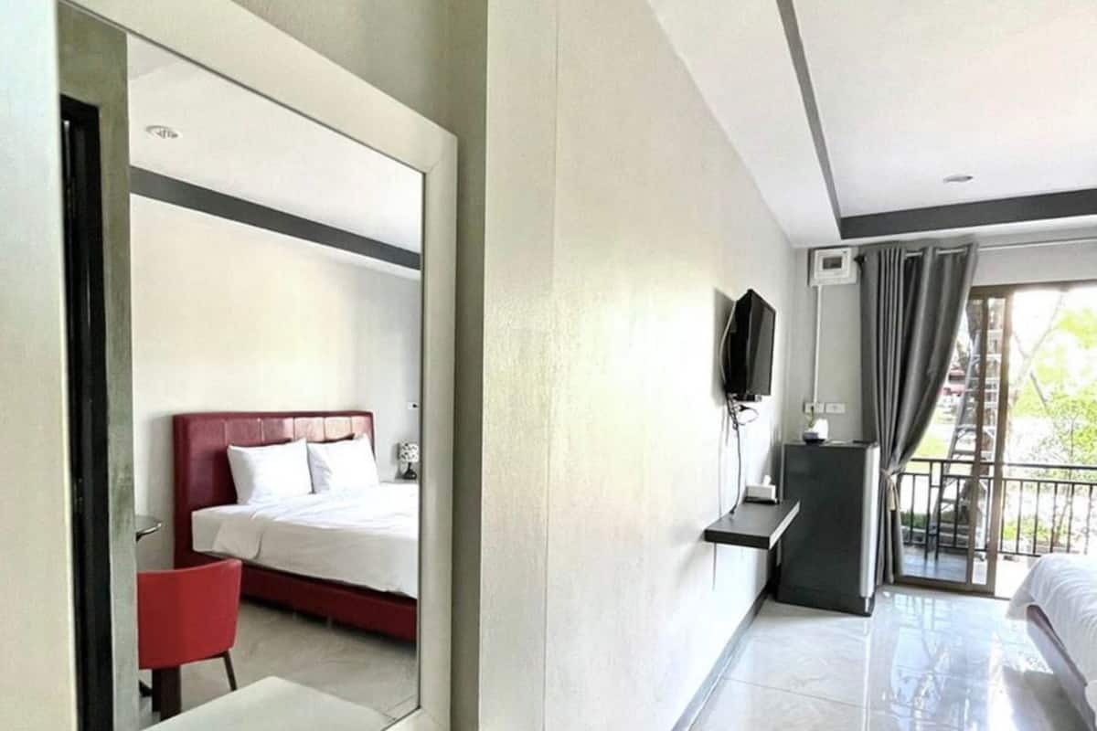 A modern hotel room with a large mirror, a red chair, a bed, a TV, and a balcony with curtains.