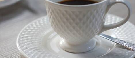 Una taza de cerámica blanca con un diseño texturizado, llena de un líquido oscuro, probablemente café, sobre un platillo y cuchara a juego.