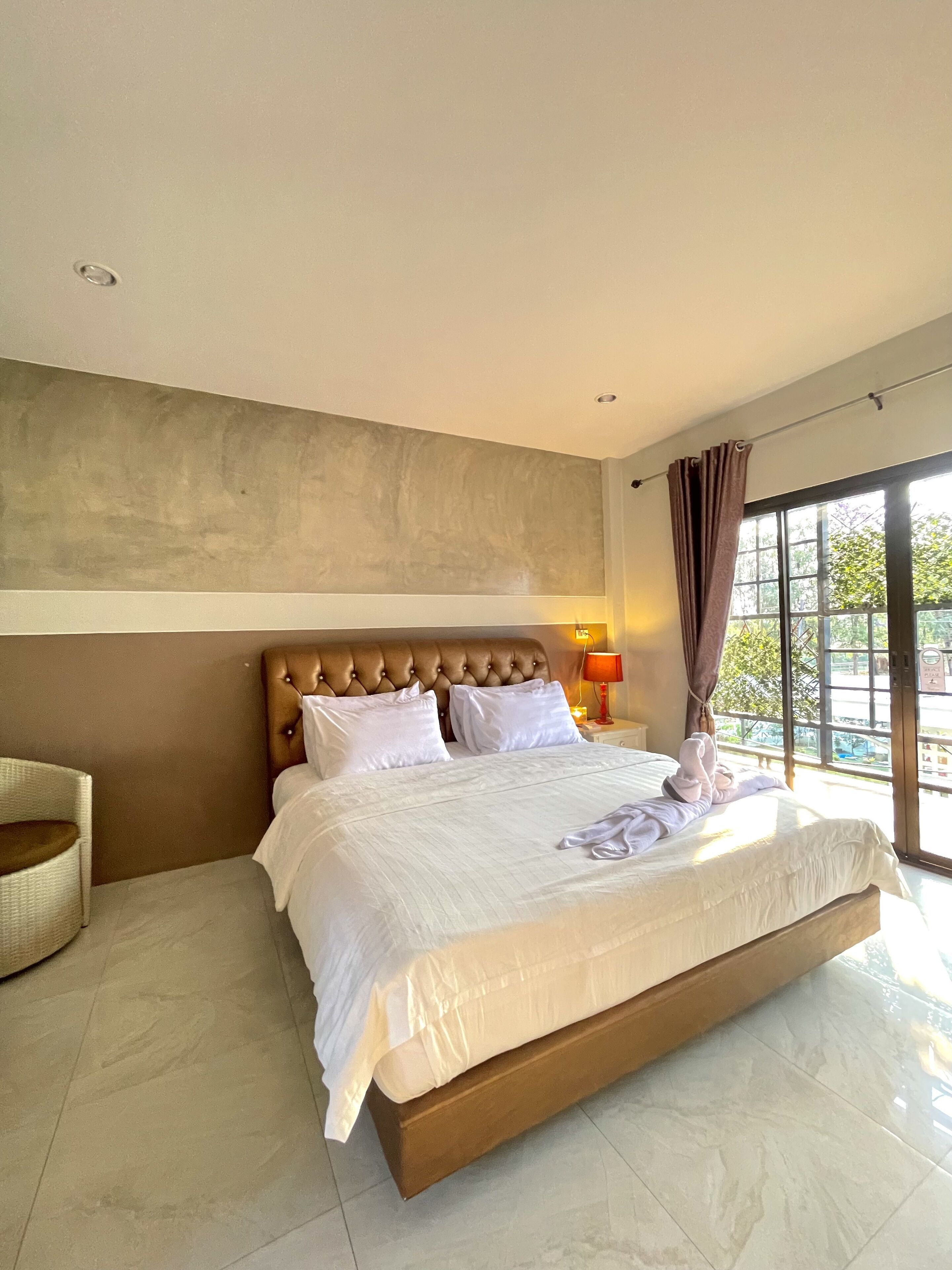 Een hotelkamer met een groot bed, een hoofdeinde, een nachtkastje, een lamp en uitzicht op het omliggende landschap.