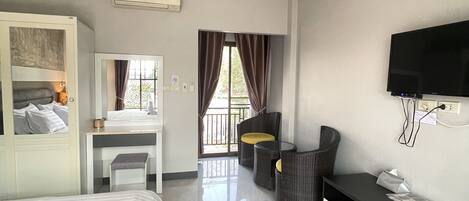 A hotel room with a bed, a desk, a chair, a TV, and a balcony with curtains.