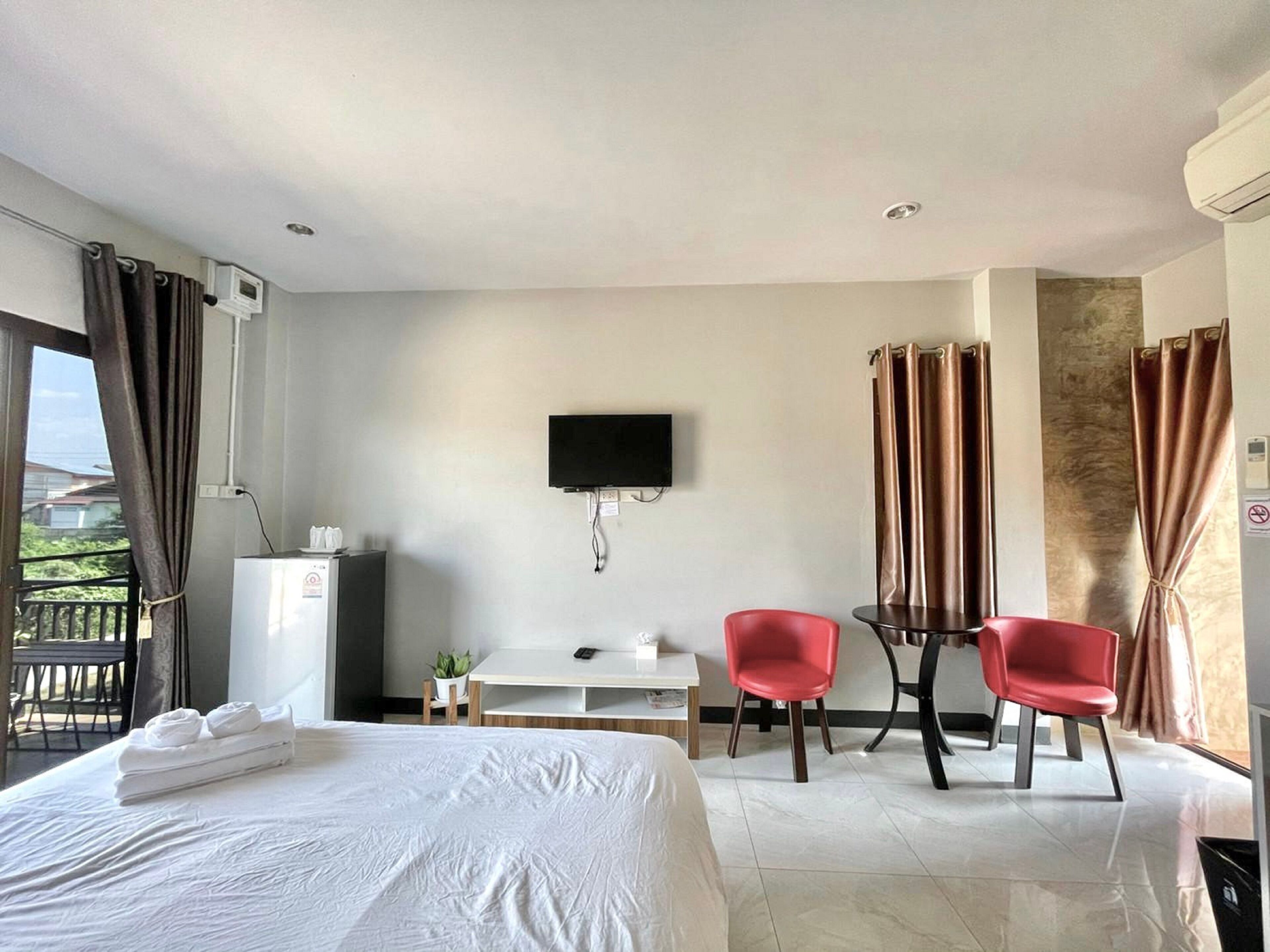 Hotelkamer met een bed, bureau, twee rode stoelen, televisie en een balkon met gordijnen.