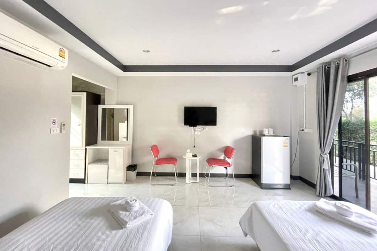 A hotel room with two beds, a desk, a TV, and a balcony with curtains.