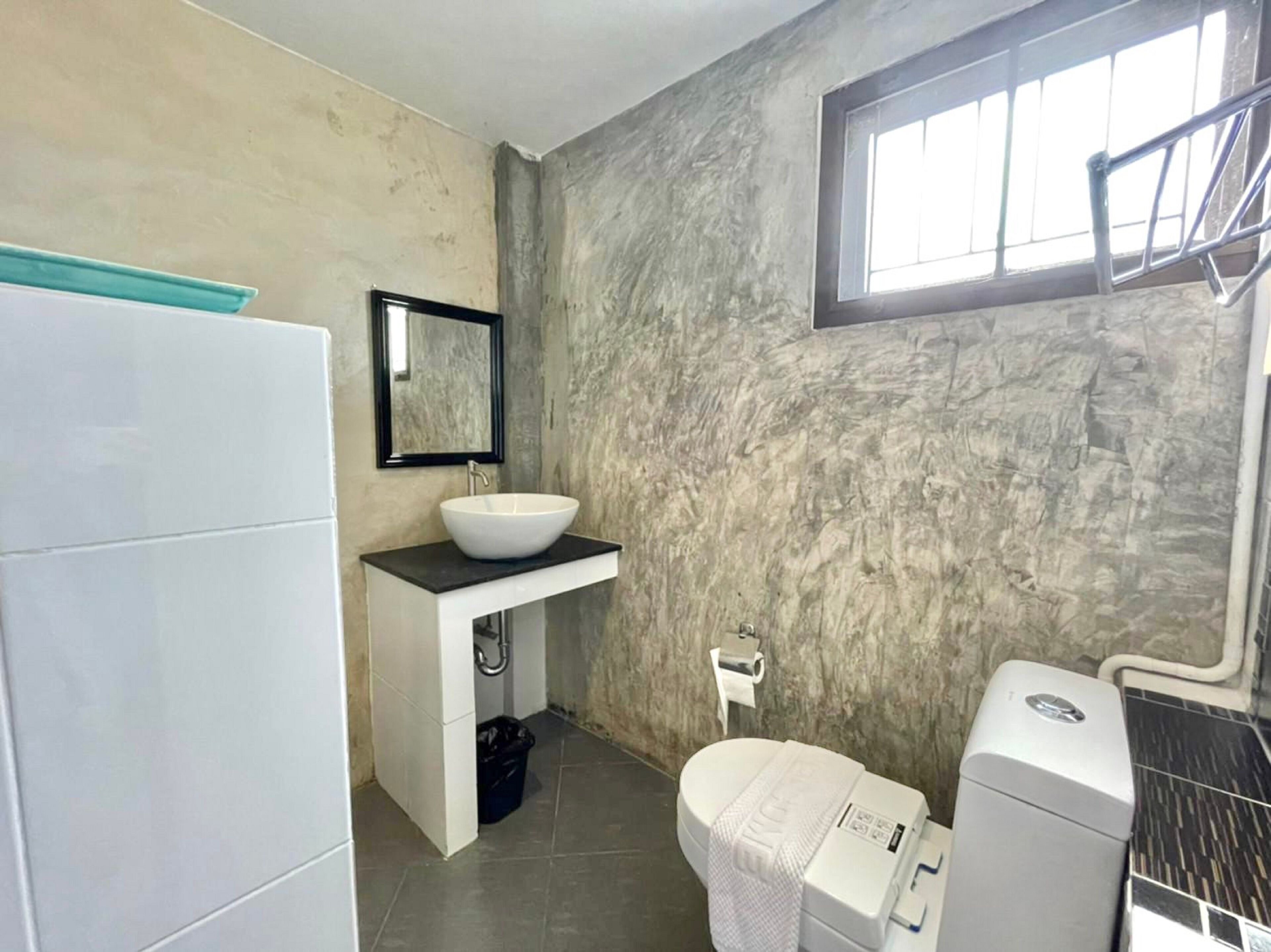A bathroom with a white sink, a mirror, a toilet, and a window.
