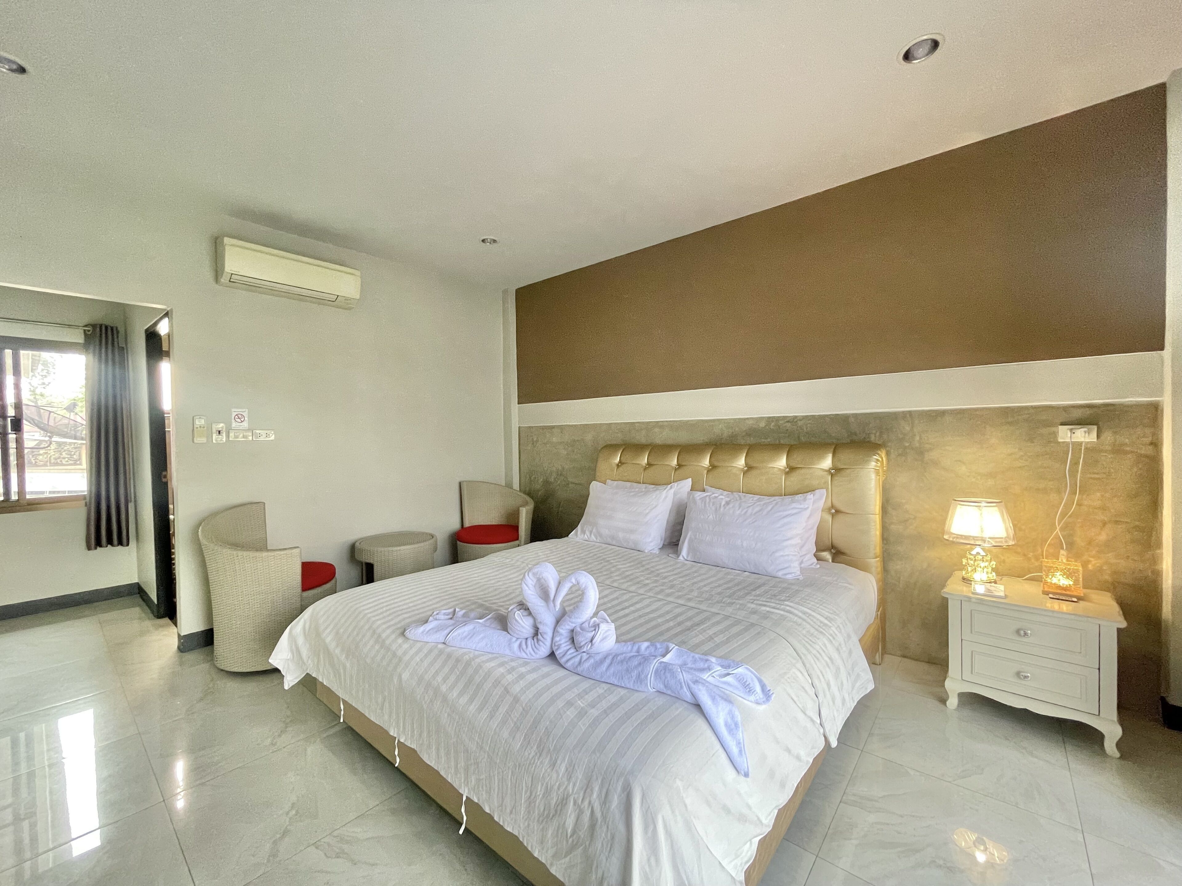A hotel room with a large bed, a bedside table with a lamp, a chair, and a small table.