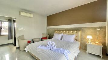 A hotel room with a large bed, a bedside table with a lamp, a chair, and a small table.