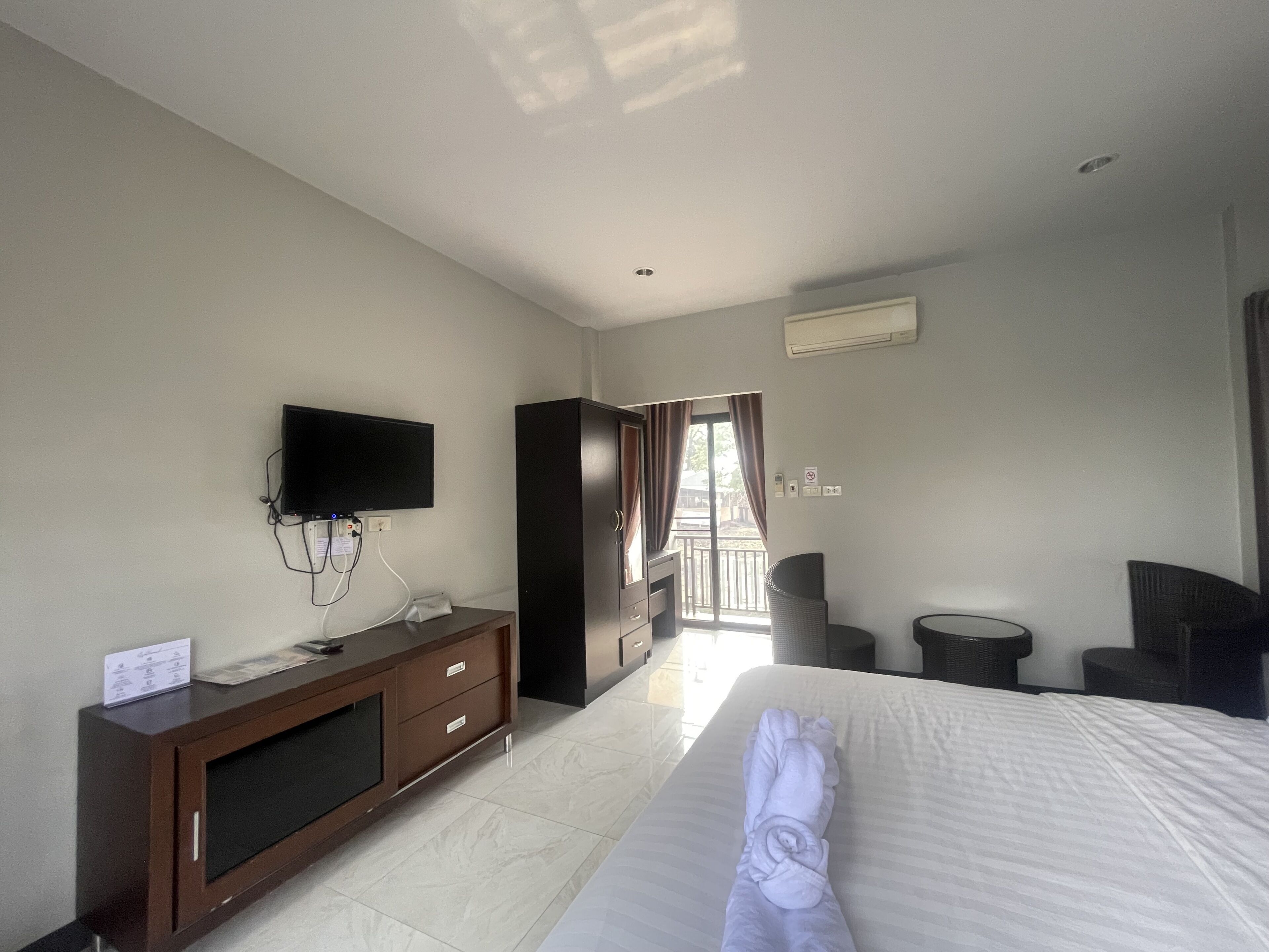 A hotel room with a bed, a TV mounted on the wall, a desk, and a wardrobe.