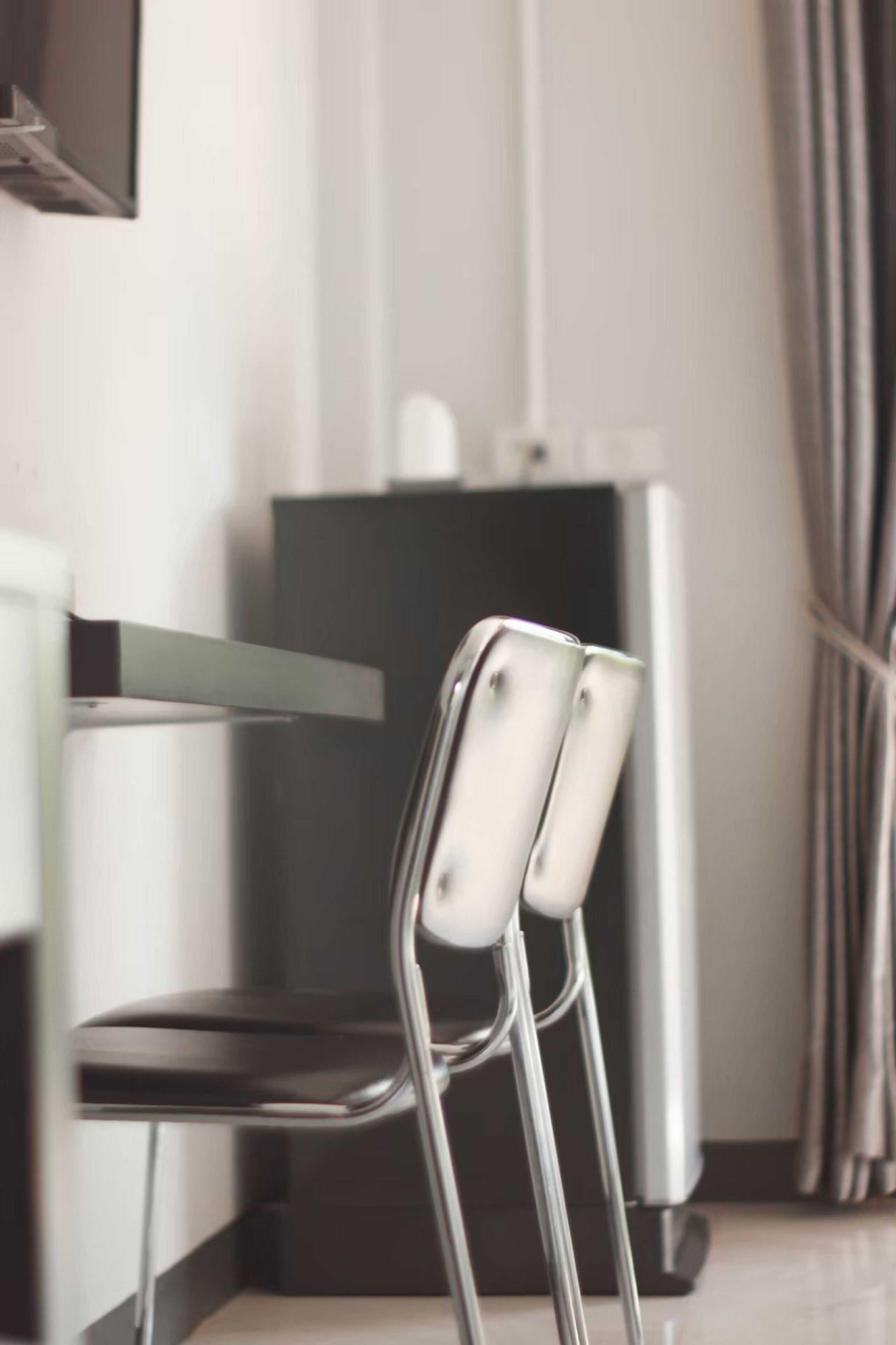 A modern kitchen with a stainless steel refrigerator, a white countertop, and a chair with a metal frame.