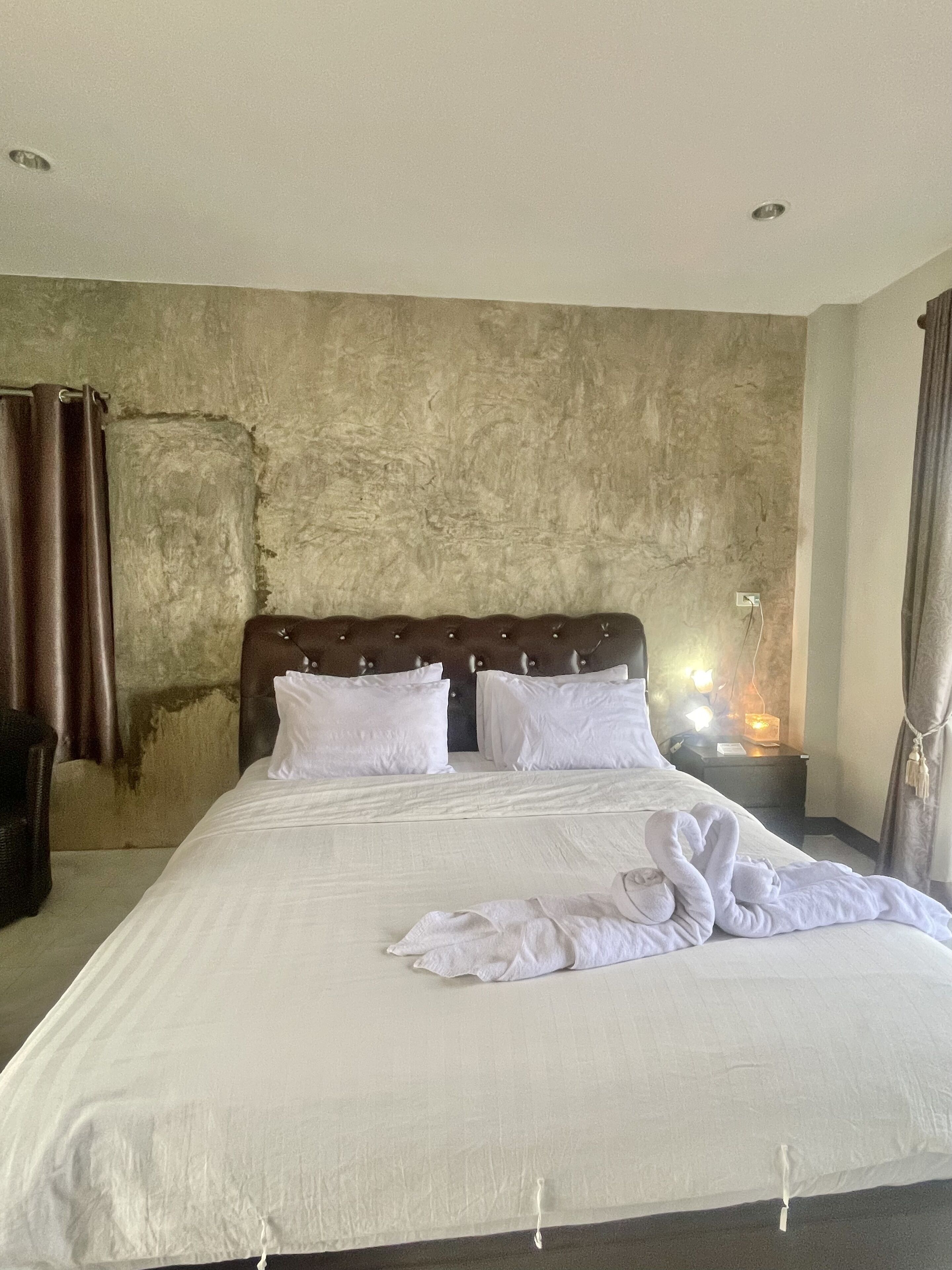 A hotel room with a large bed, a headboard, a nightstand with a lamp, and a curtain.