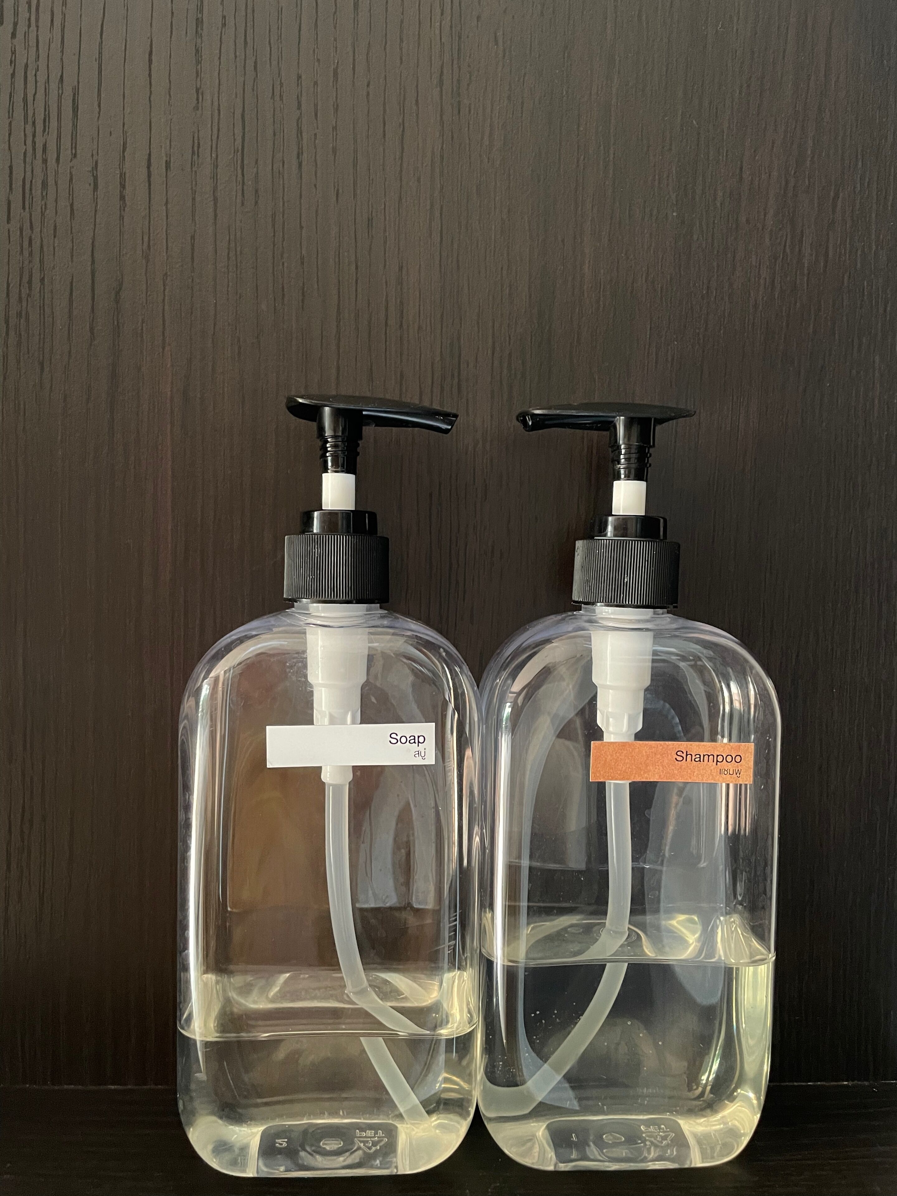 Two clear plastic bottles with pump dispensers, one labeled 'Soap' and the other 'Shampoo', against a dark wooden background.