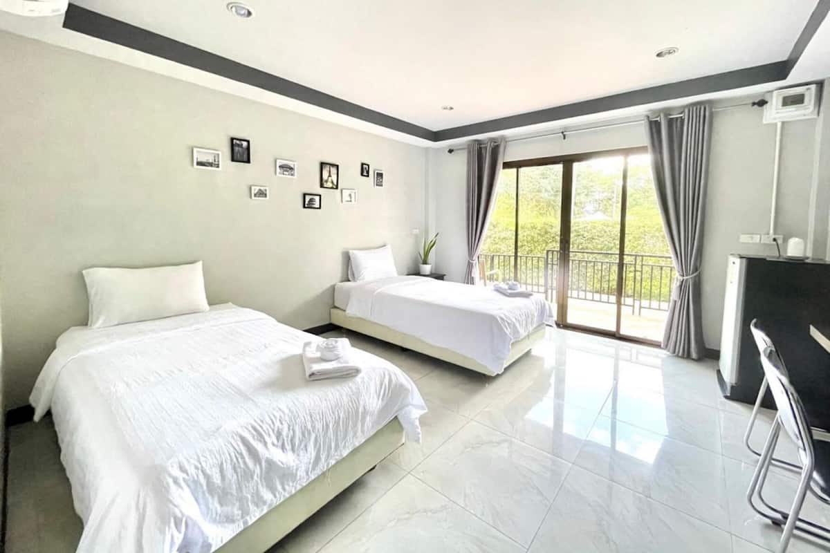 A hotel room with two beds, a balcony with curtains, a desk, and a chair.