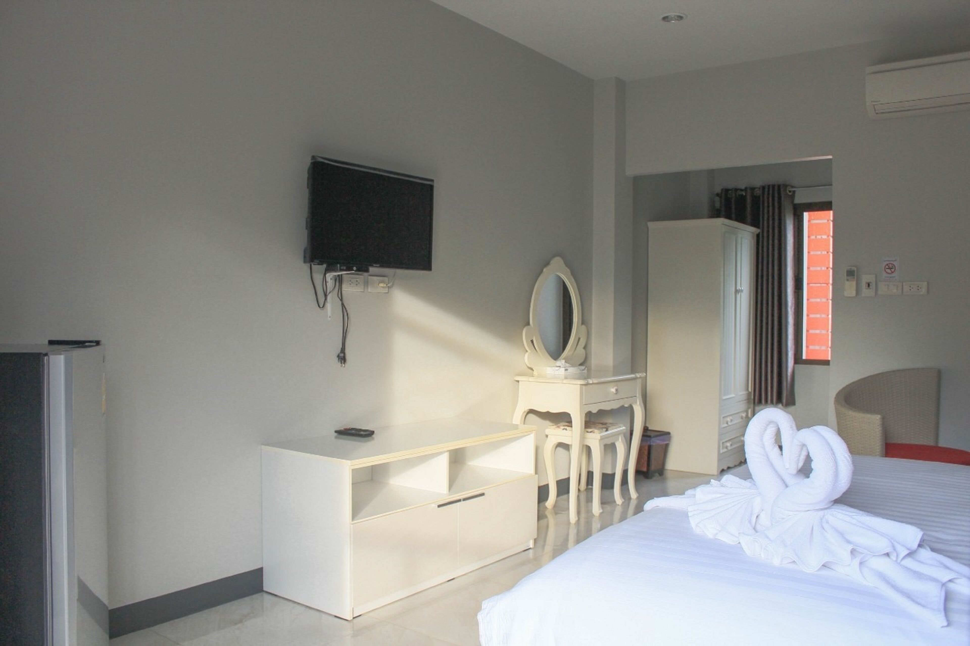 Een hotelkamer met een bed, een aan de muur bevestigde televisie, een kaptafel met spiegel en een kledingkast.