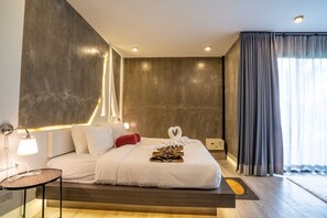 A modern hotel room with a large bed, bedside lamps, and a view of the outdoors through a window with curtains. - Phi Phi Andaman Legacy Resort (Ko Phi Phi)