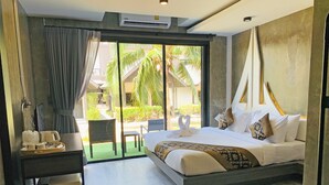 A modern hotel room with a large bed, a desk with a tray of breakfast items, a chair, and a view of a courtyard with palm trees. - Phi Phi Andaman Legacy Resort (Ko Phi Phi)