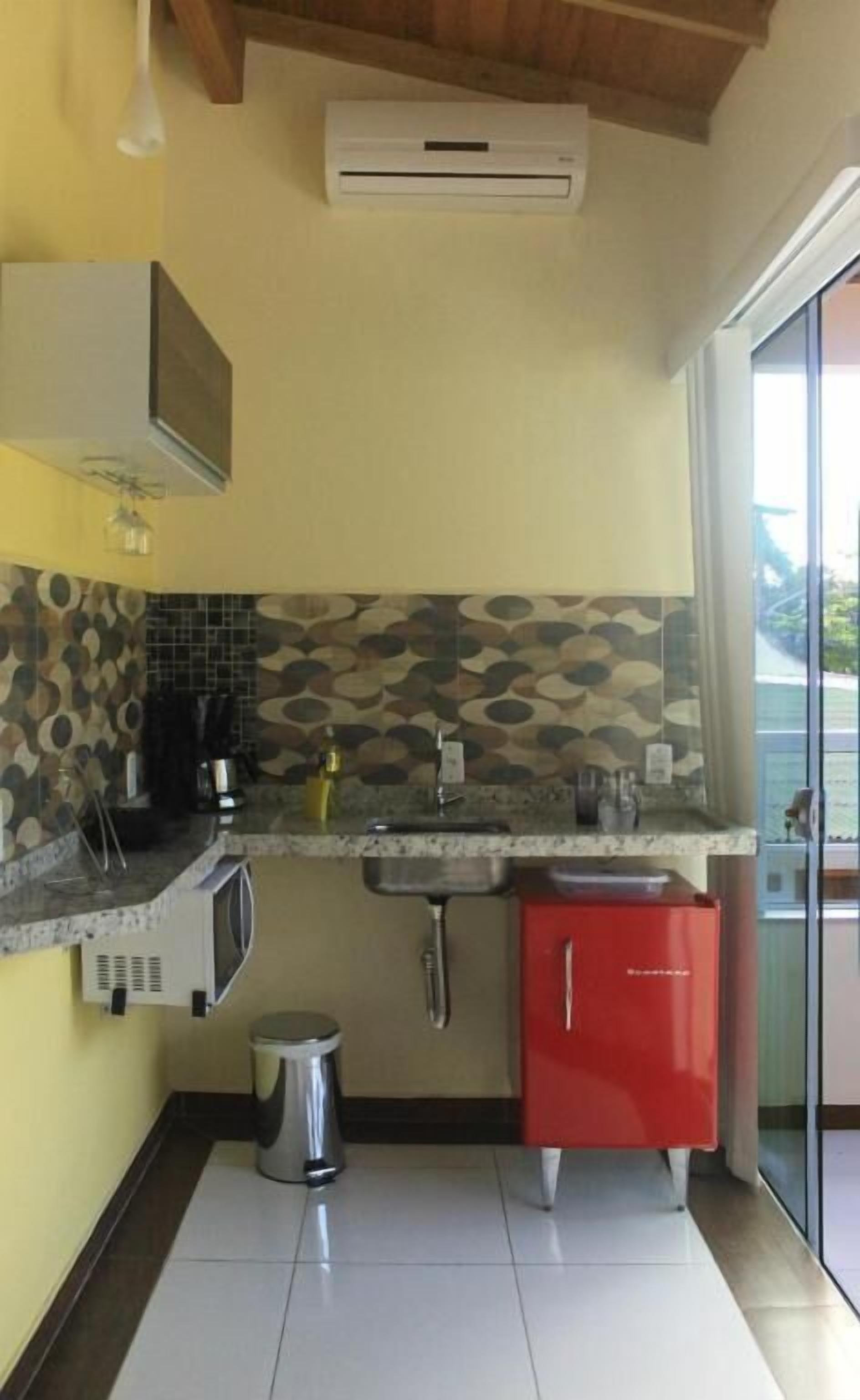 A compact kitchen with a tiled backsplash, a sink, a red cabinet, and a trash bin.