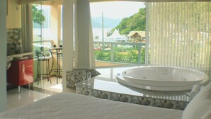A bedroom with a large bed, a bathroom with a bathtub, and a balcony with a view of the landscape. - Pousada Ilha da Magia (Florianópolis)