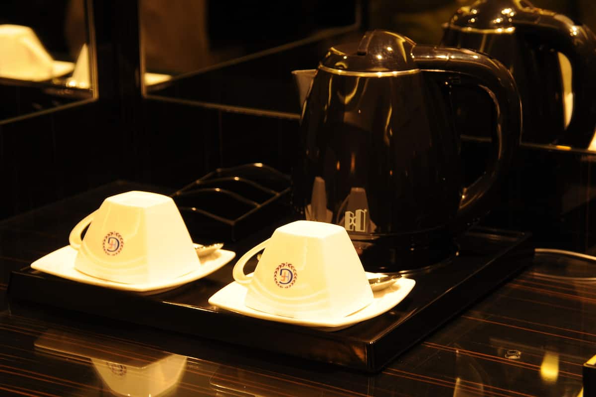 A kitchen area with a black stove, two white cups with lids, and a black electric kettle.
