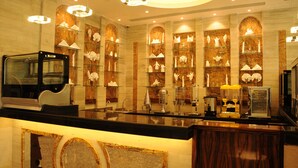 A hotel reception area with a marble wall, glass display shelves, a black reception desk, and a chandelier. - Frsan Palace Hotel (Manama)